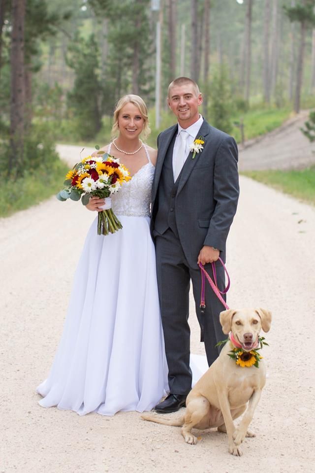 A bride and groom are posing for a picture with their dog.
