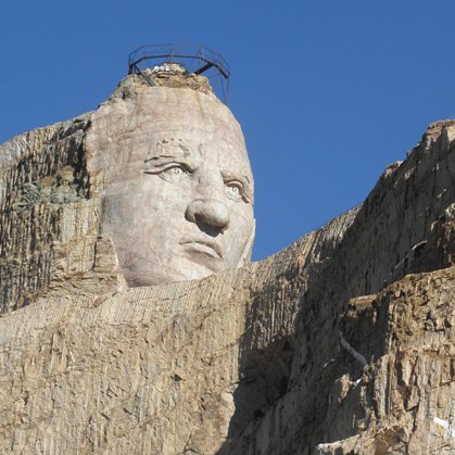 A large statue of a man 's face on top of a rocky cliff
