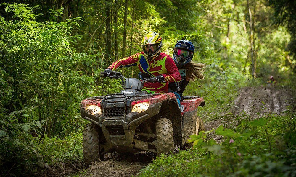 A man and a woman are riding an atv through the woods.