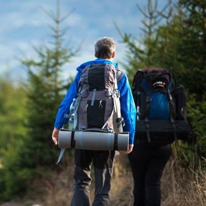 A man and a woman with backpacks are walking down a path.