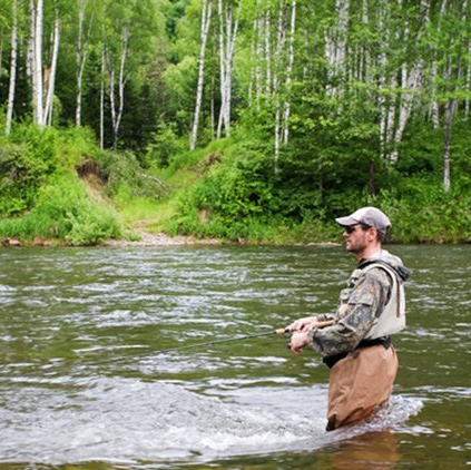 A man is fishing in a river with trees in the background