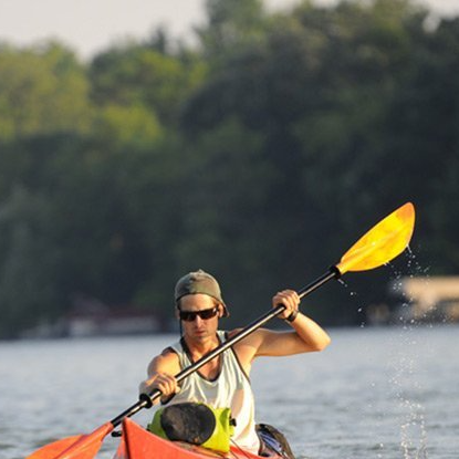 A man is paddling a red kayak with a yellow paddle