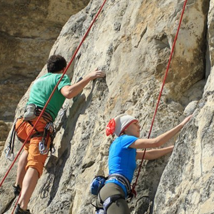 A man and a woman are climbing up a rock wall