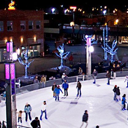 A group of people are ice skating on a rink at night