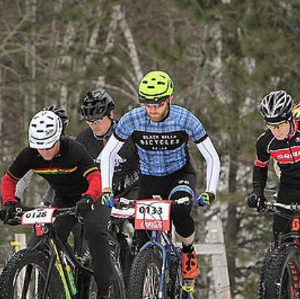 A group of men are riding bicycles in the snow.