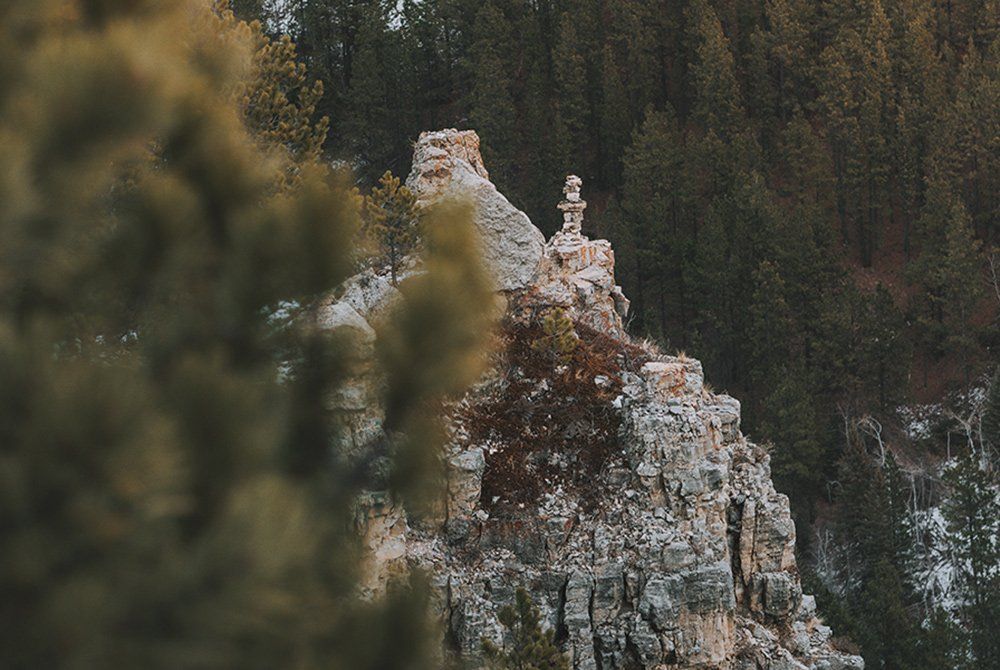 A rocky cliff with a cross on top of it in the middle of a forest.