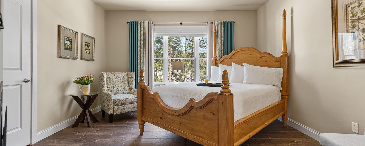 A bedroom with a four poster bed , chair , table and window.