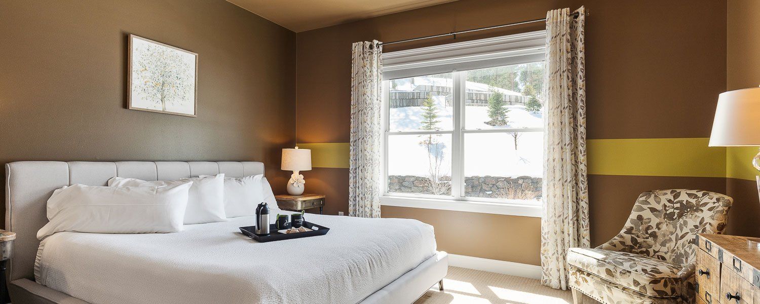 A bedroom with a large bed , chair , lamp and window.