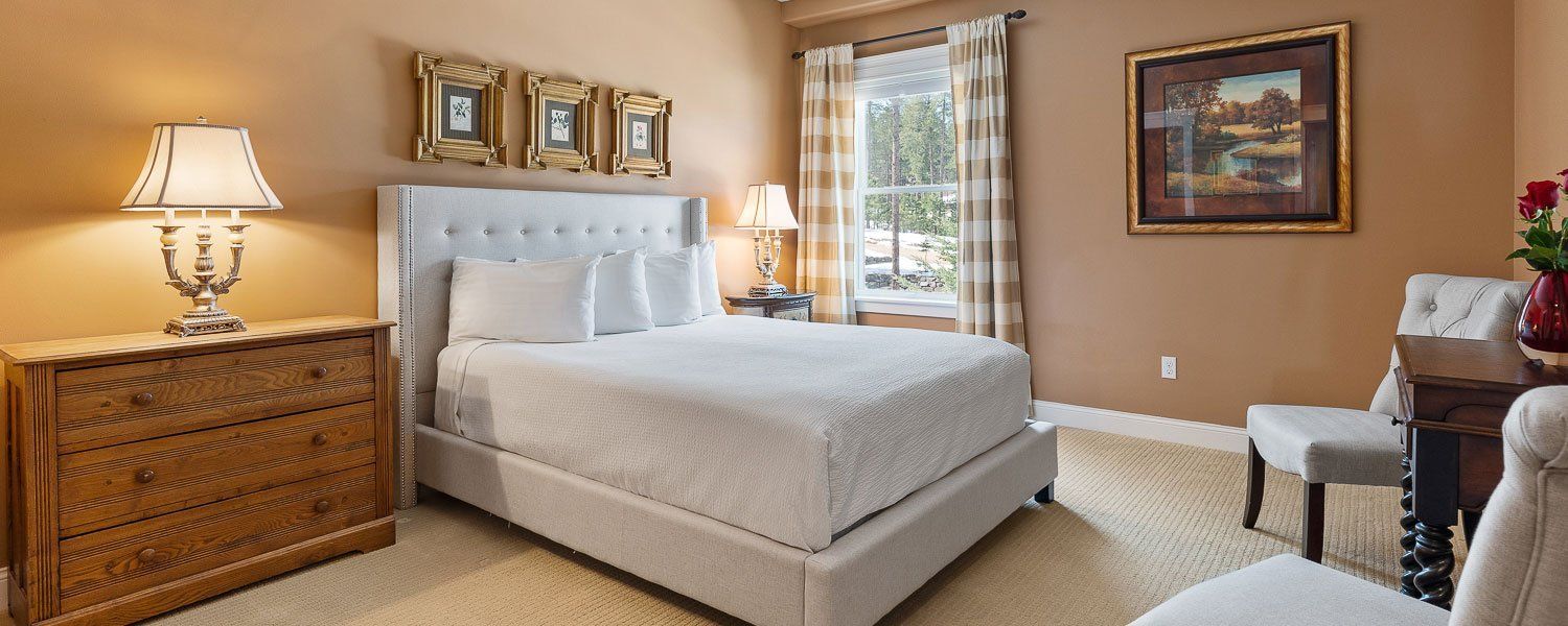 A bedroom with a bed , dresser , chairs and lamps.