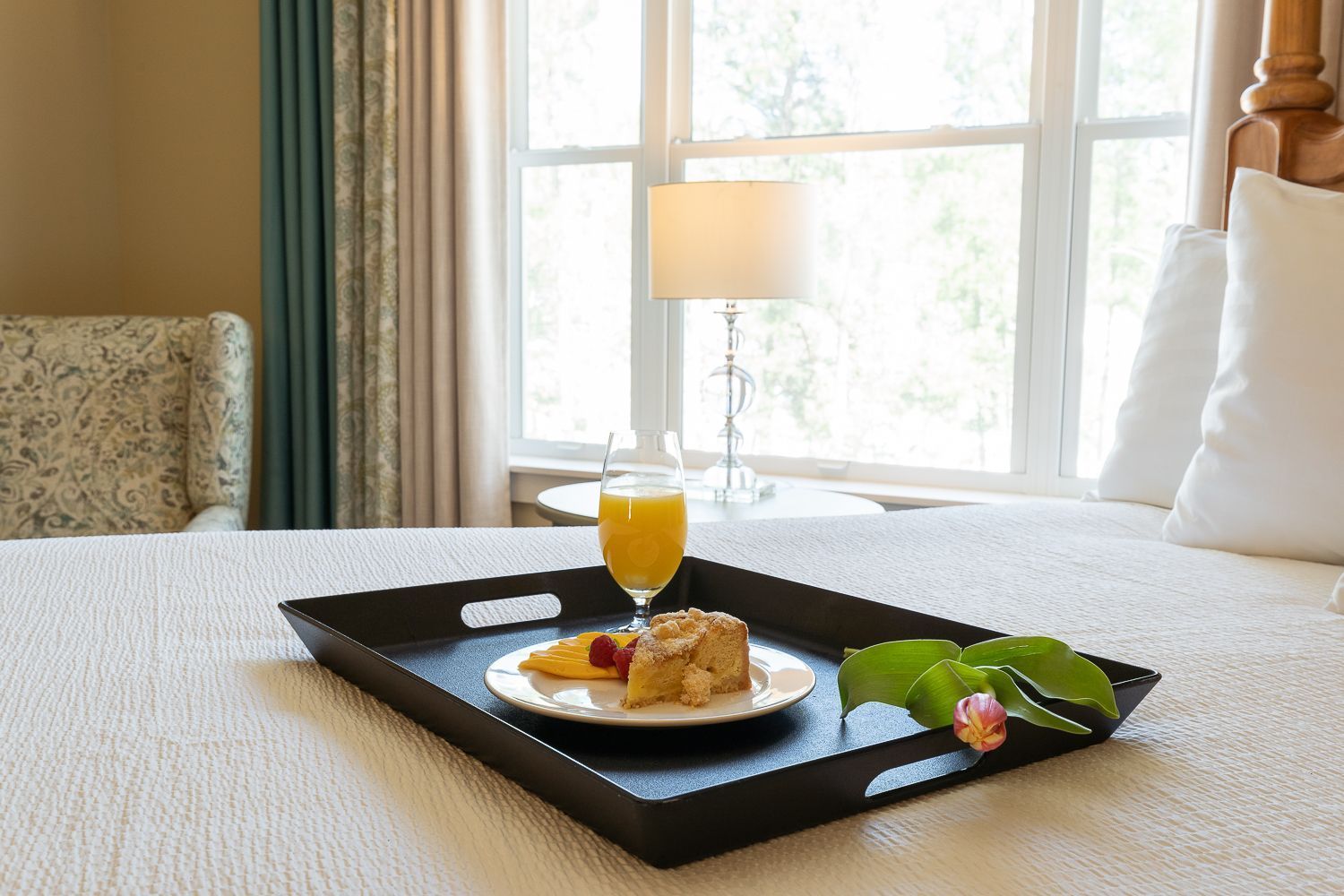 A tray of food and a glass of orange juice on a bed.