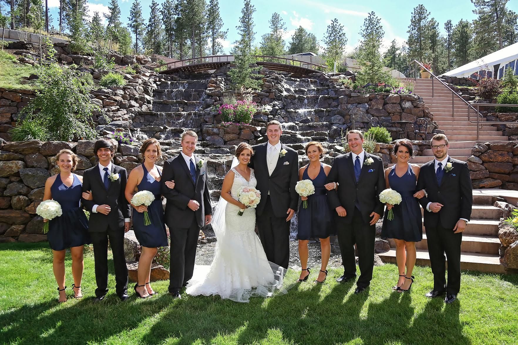 A bride and groom pose with their wedding party in front of a waterfall.