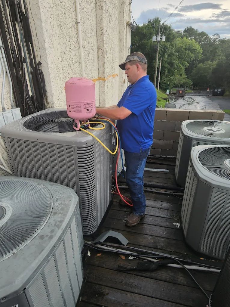 HVAC technician working on an air conditioning unit on a rooftop. Wearing blue shirt, using pink equipment.