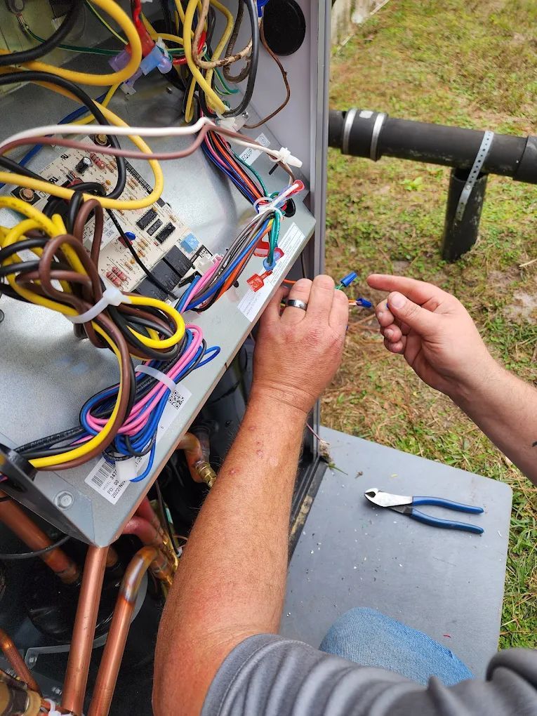 A person is working on AC unit wiring with pliers outdoors.