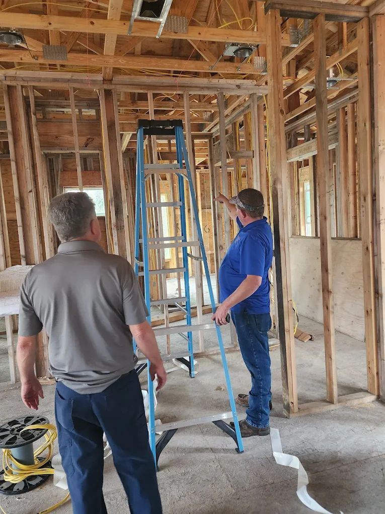 Two men at a construction site; one points near a ladder, wooden frame interior.