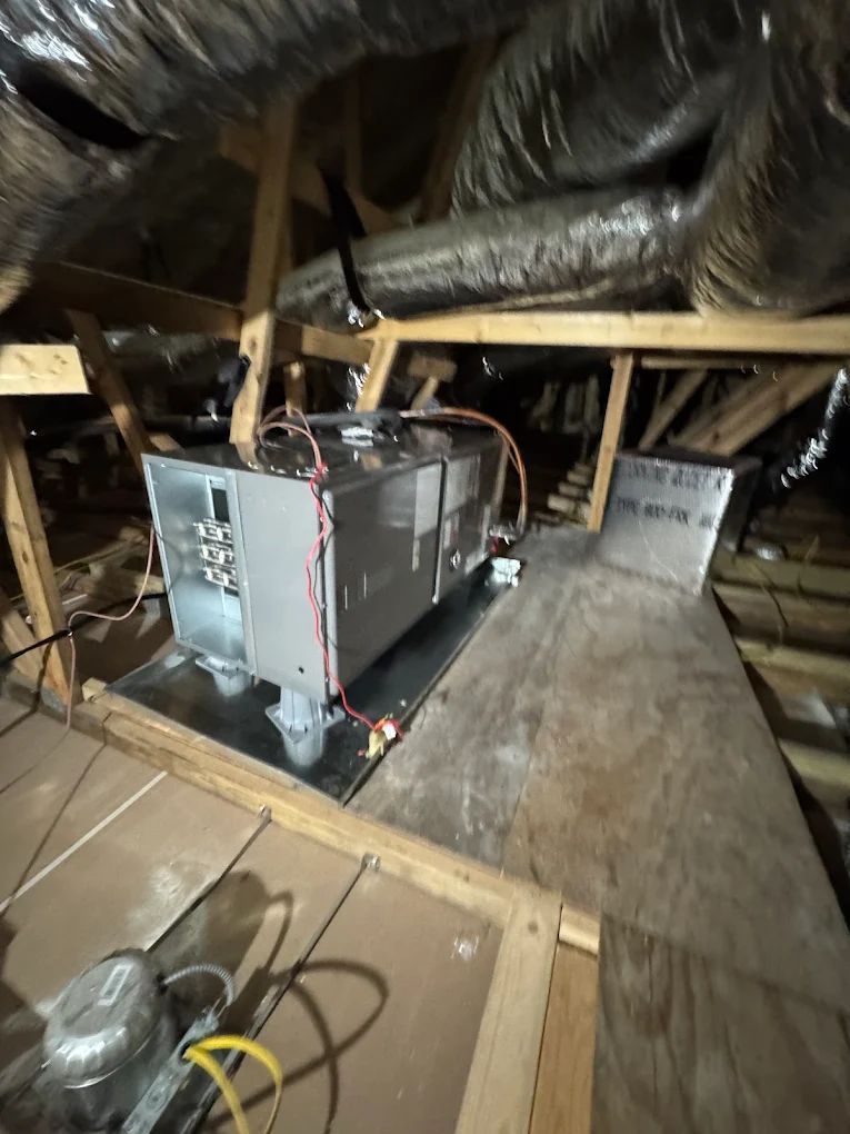 HVAC unit in an attic, on a wooden platform. Ductwork overhead.