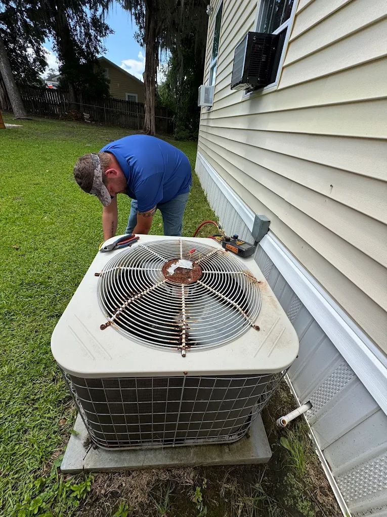 Man inspecting an outdoor air conditioning unit; grass and house in background.