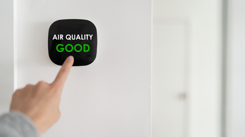Hand pointing at a black air quality monitor displaying