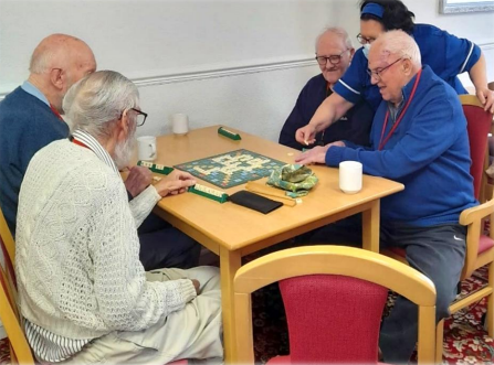 A group of elderly people sat around a table, playing a board game.