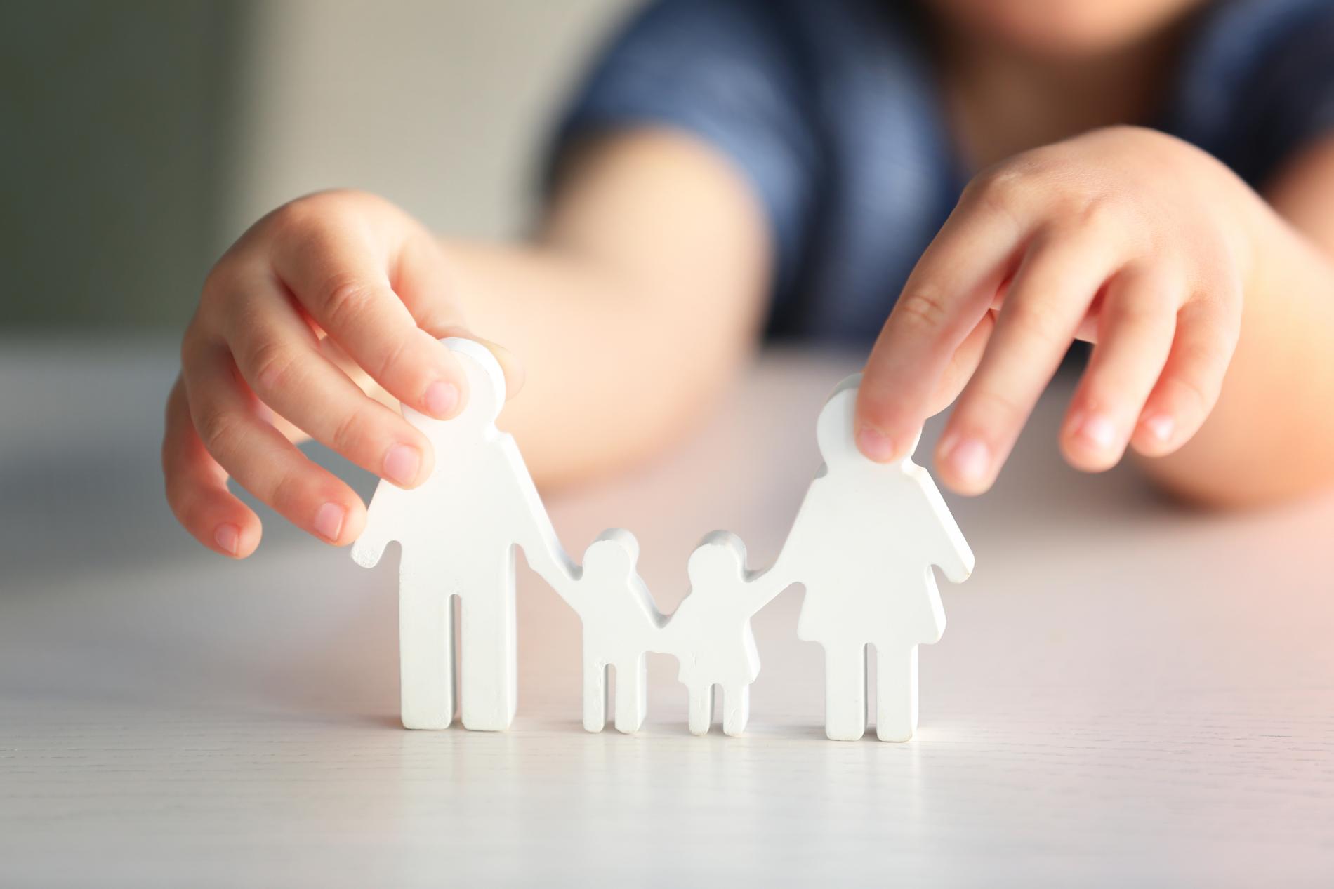 Child's hands holding white family figures, symbolizing family unity.