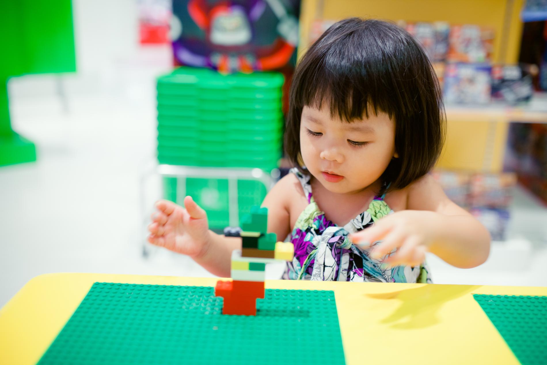 Young child with dark hair building with colorful blocks at a table.