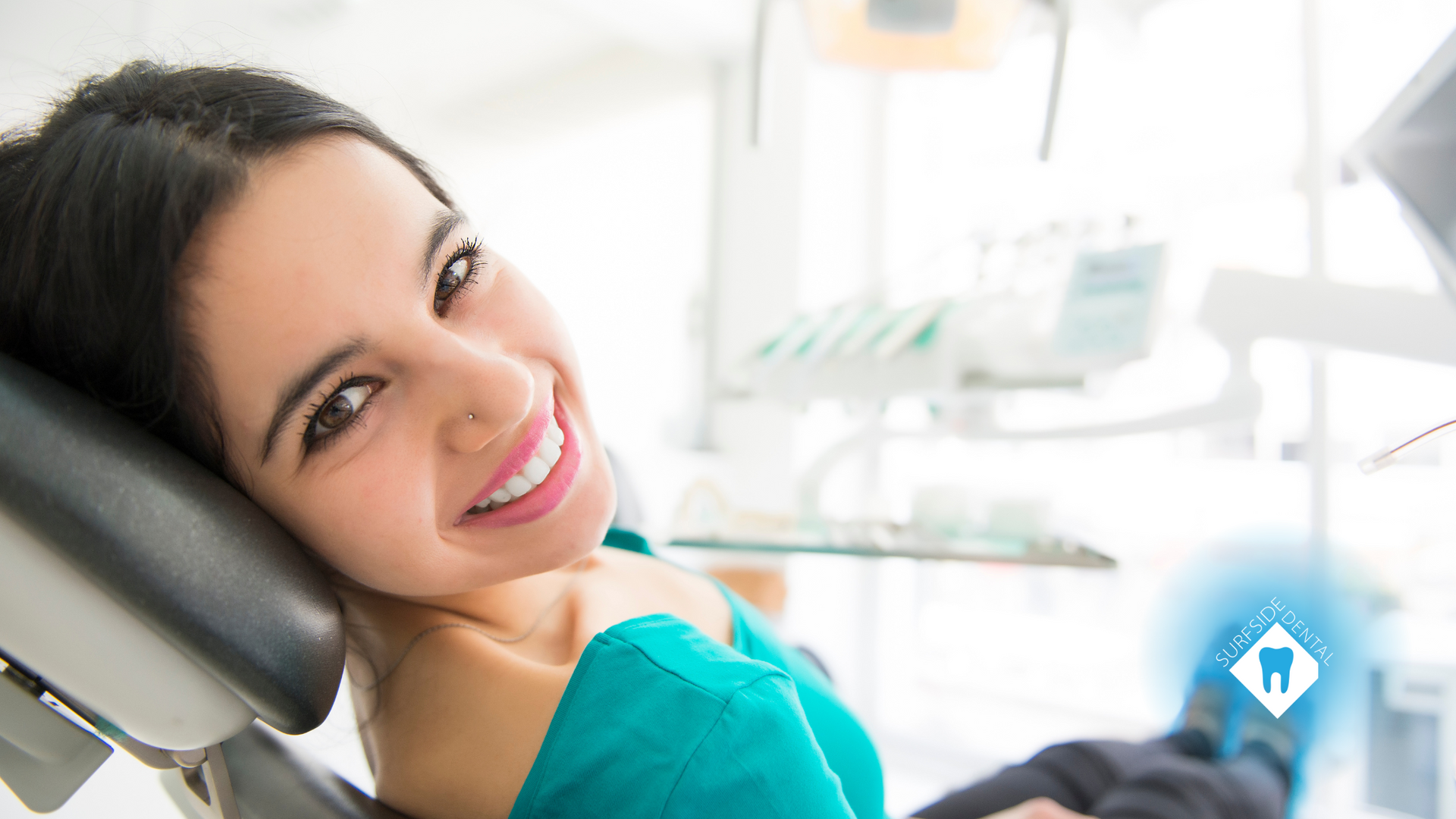 A woman is smiling while sitting in a dental chair.