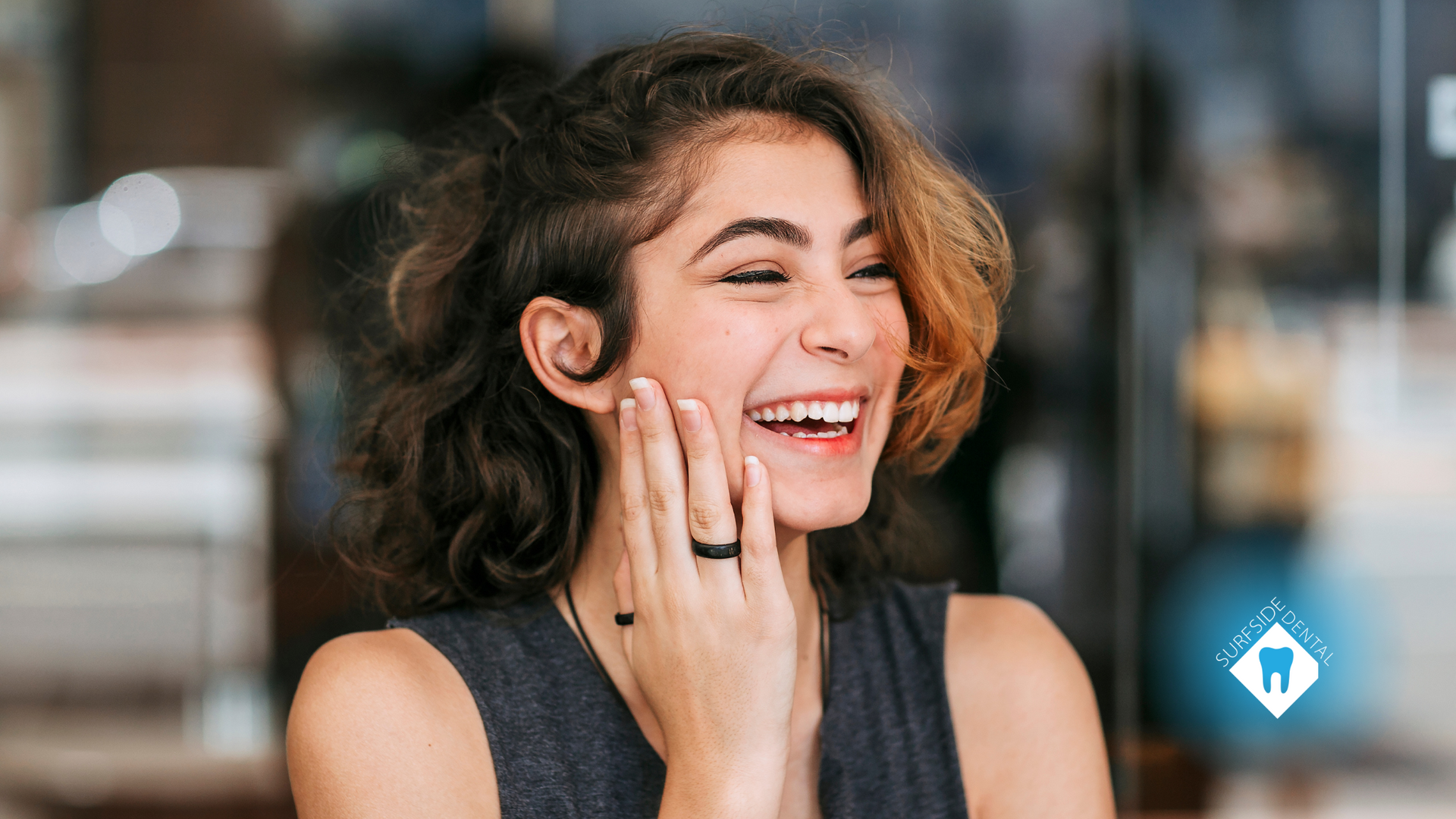 A woman is laughing with her hand on her face.