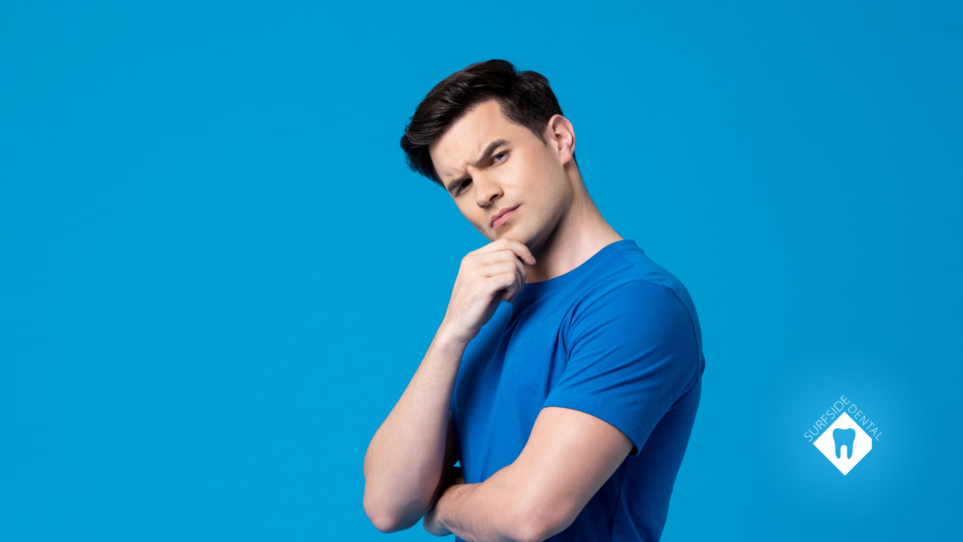 A man in a blue shirt is thinking with his hand on his chin.