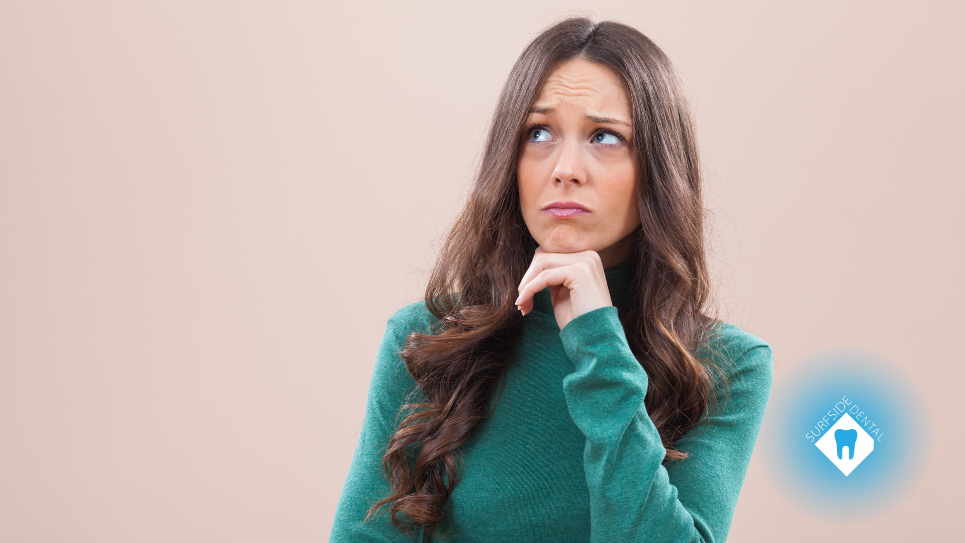 A woman in a green sweater is thinking about her teeth.