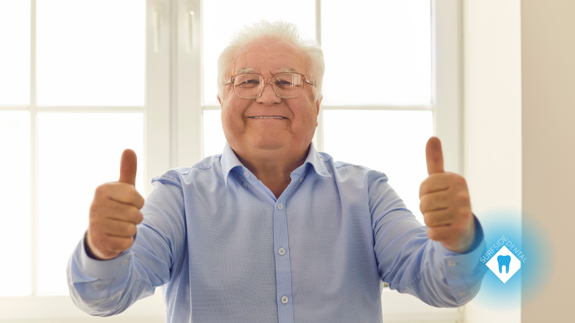 An elderly man is giving two thumbs up in front of a window.