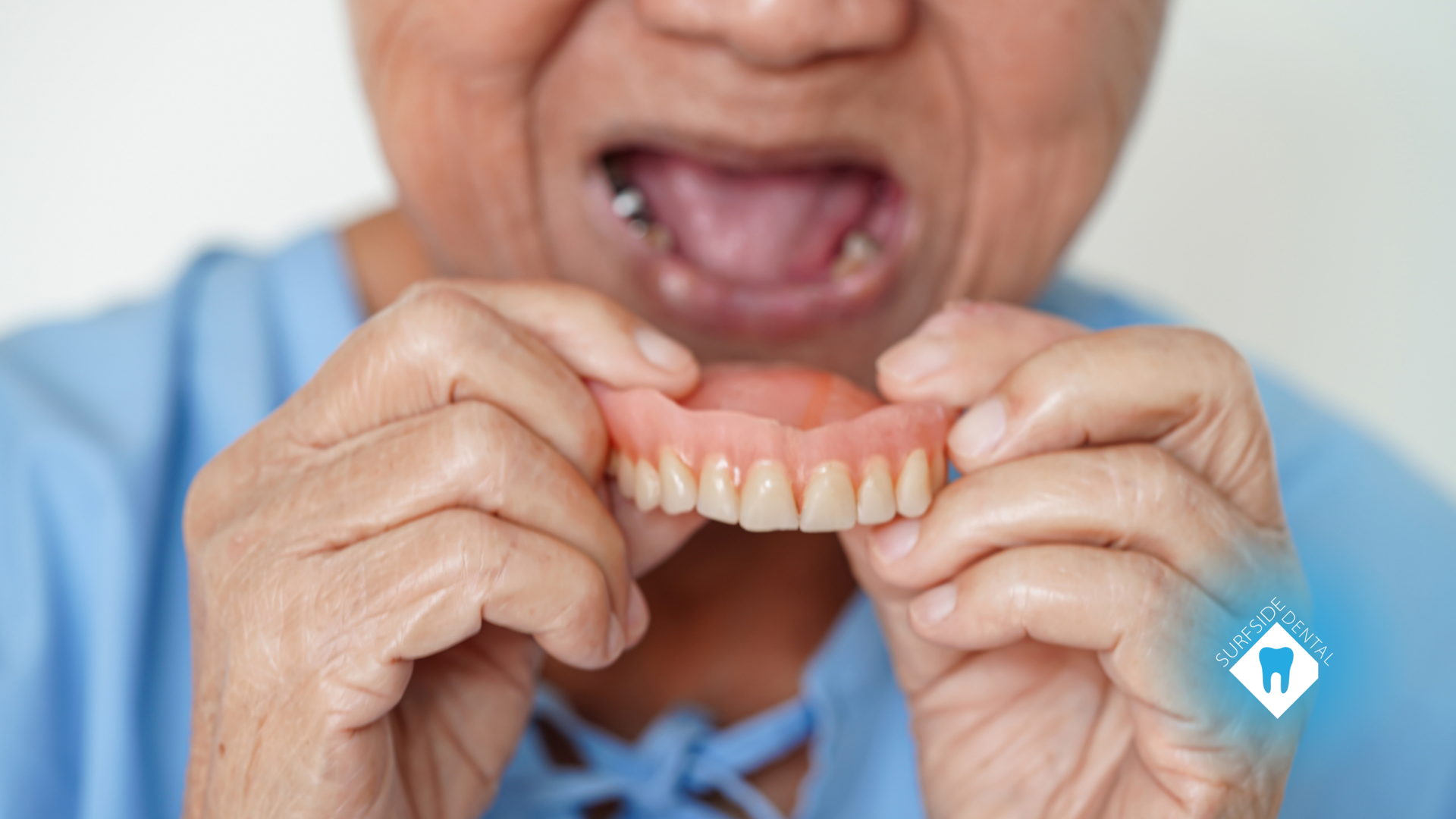 An elderly woman is holding her dentures in her hands.