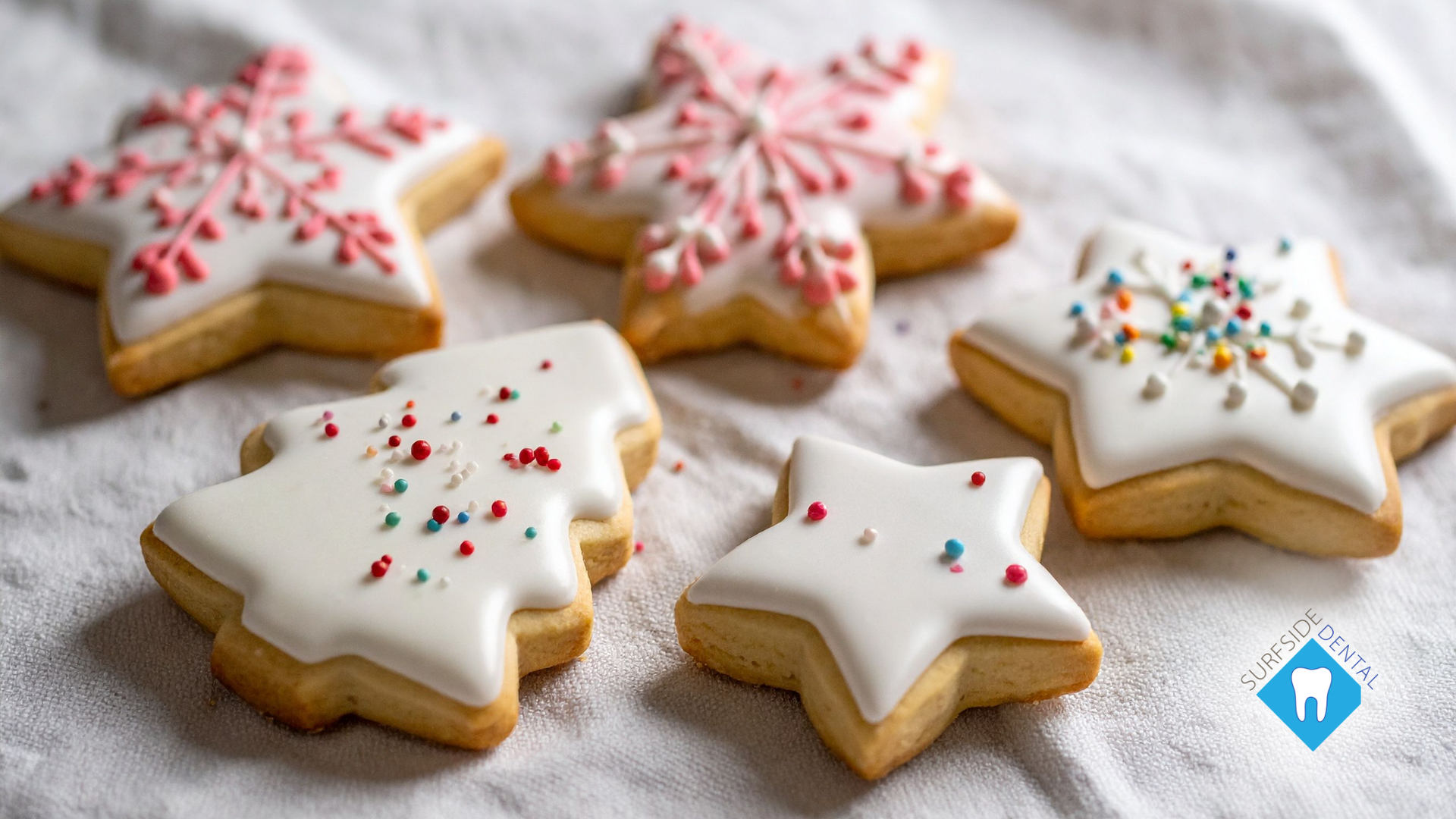 Decorated star and Christmas tree-shaped sugar cookies with white icing and sprinkles on a white cloth.
