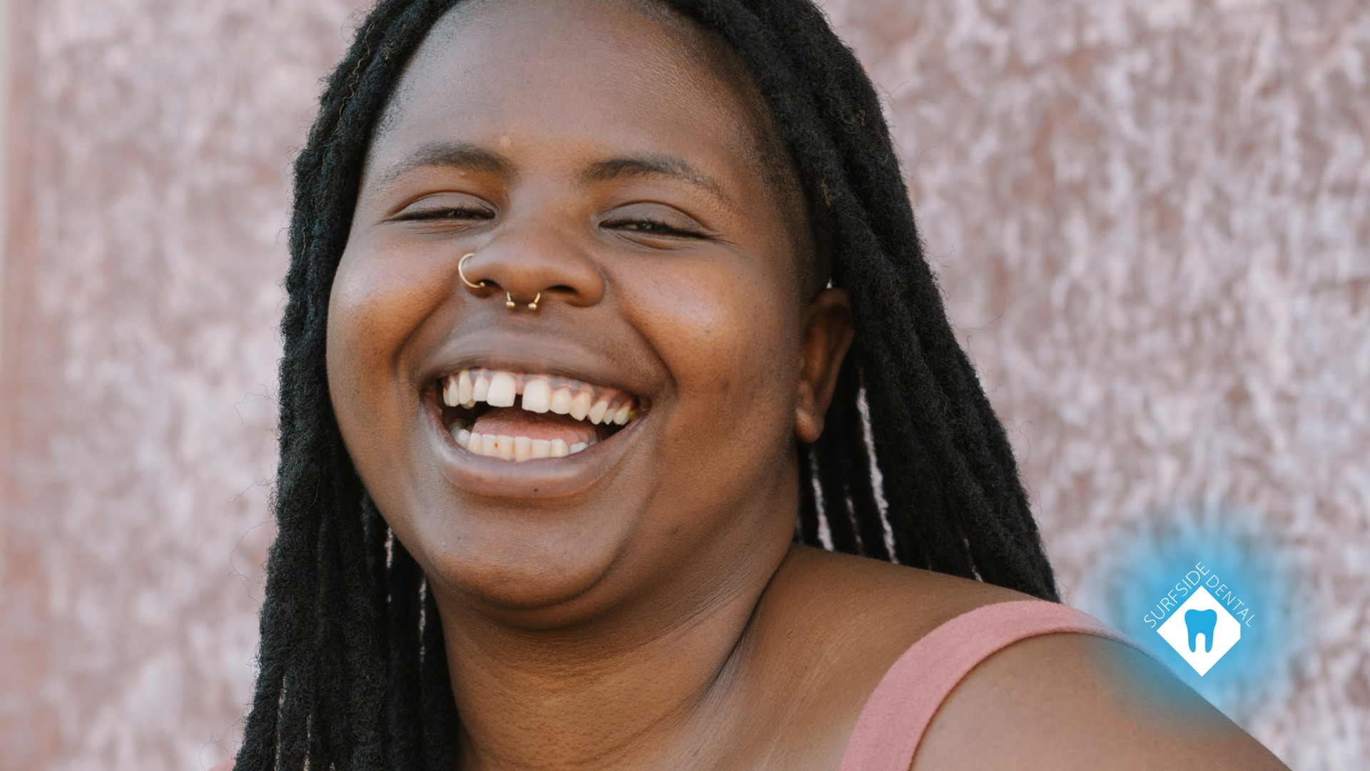 A woman with dreadlocks is laughing with her eyes closed.