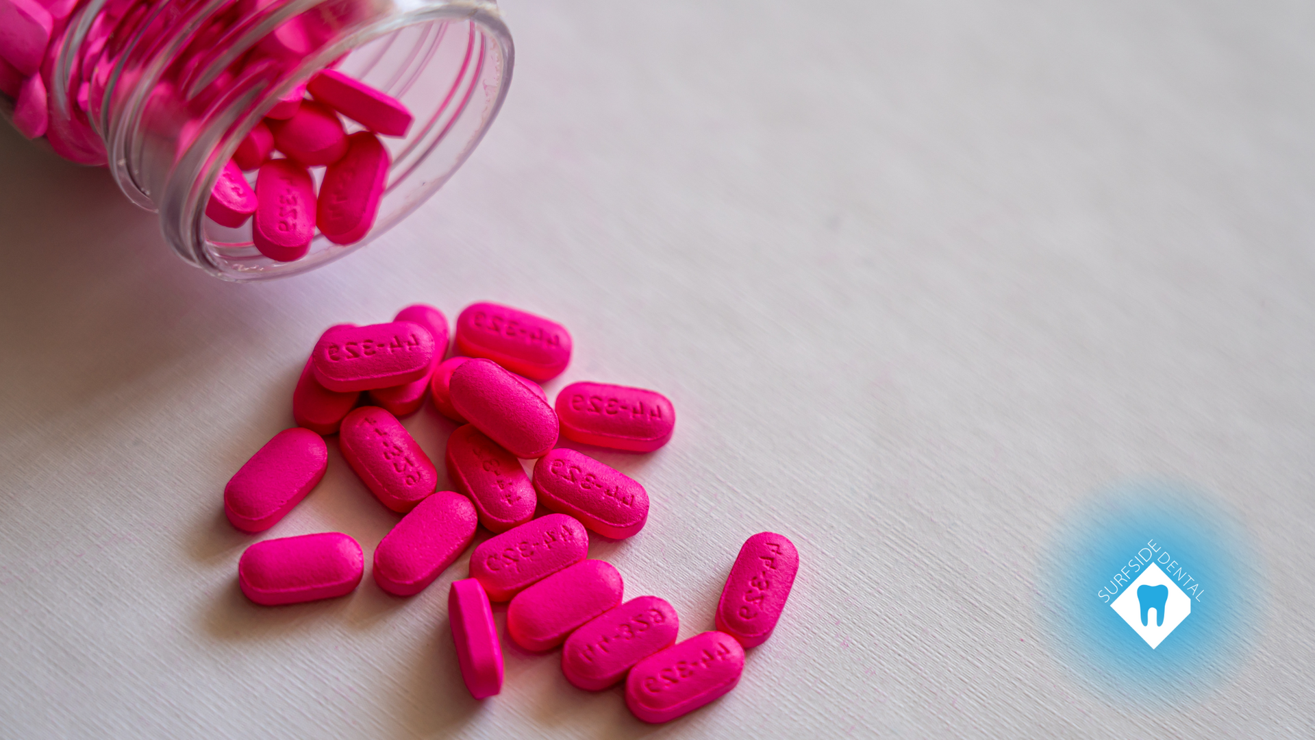 Pink pills are pouring out of a bottle on a table.