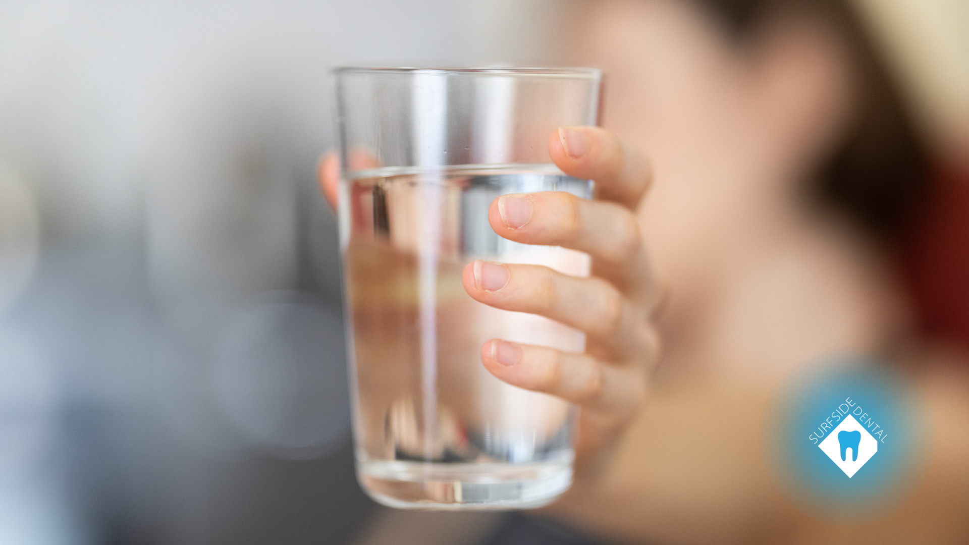 Hand holding a glass of water, blurred background.