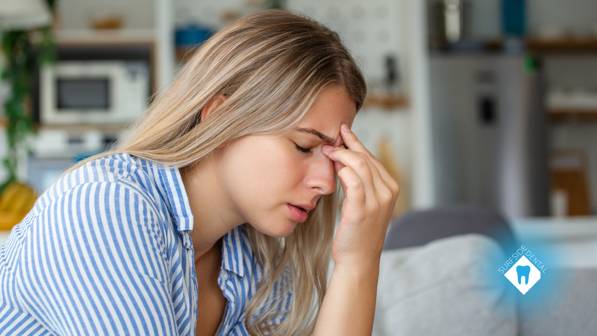 A woman is sitting on a couch with her hand on her forehead.