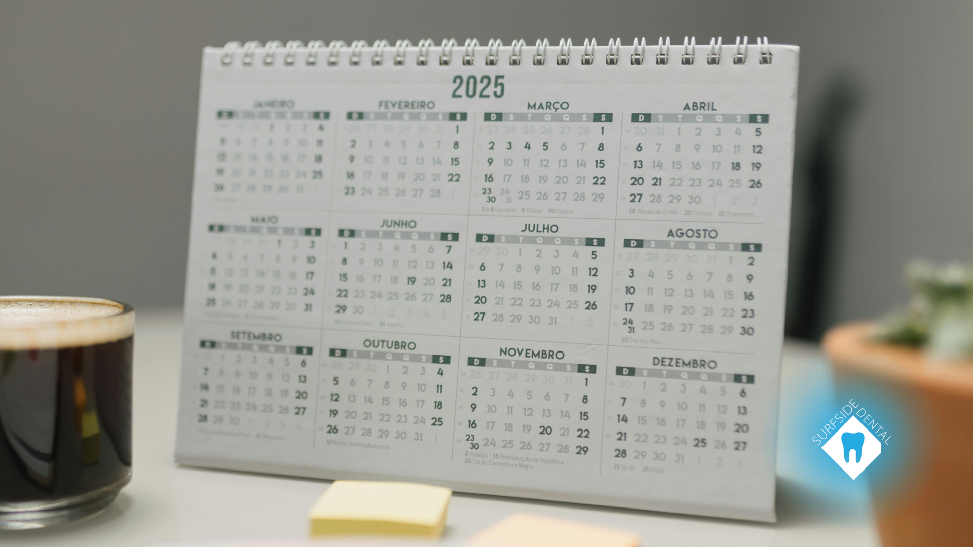 2025 calendar on a desk next to a coffee cup and sticky notes, with a plant in the background.