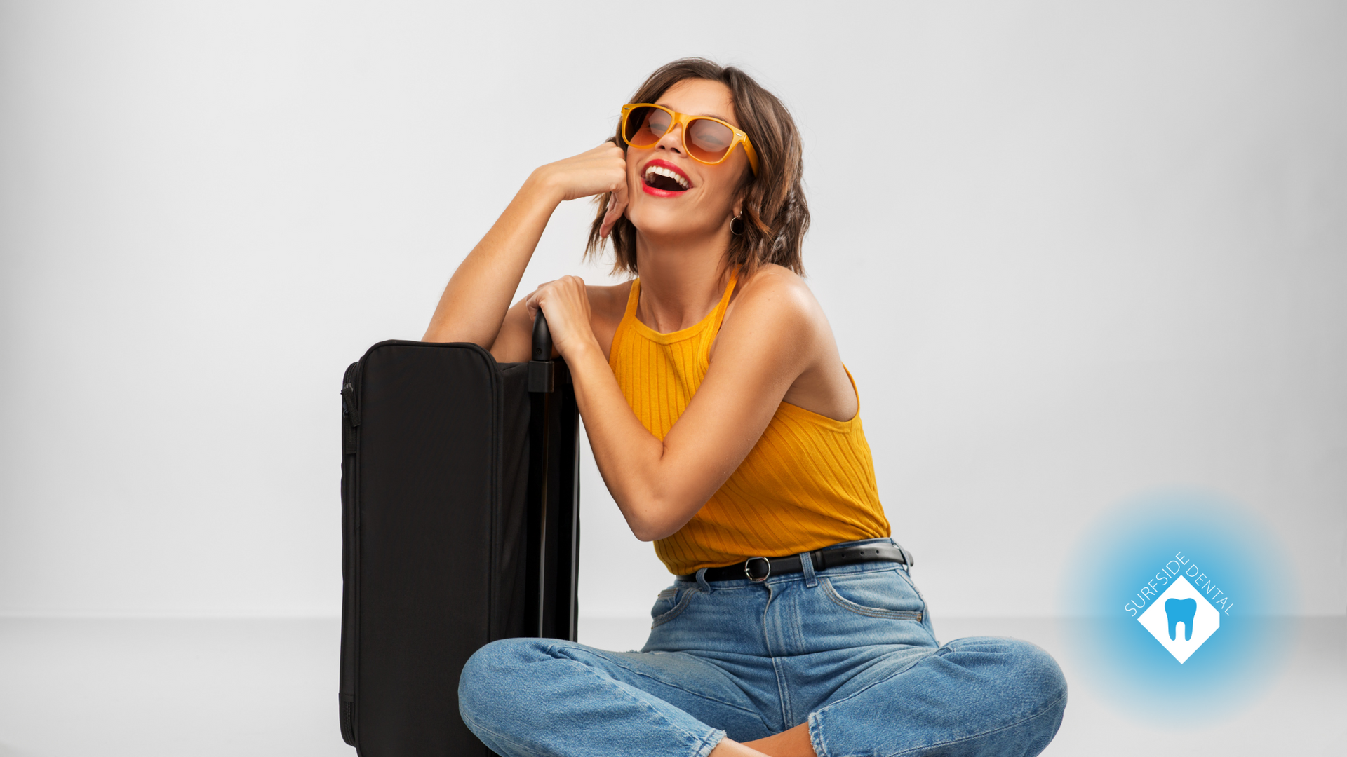 A woman is sitting on the floor with her legs crossed next to a suitcase.