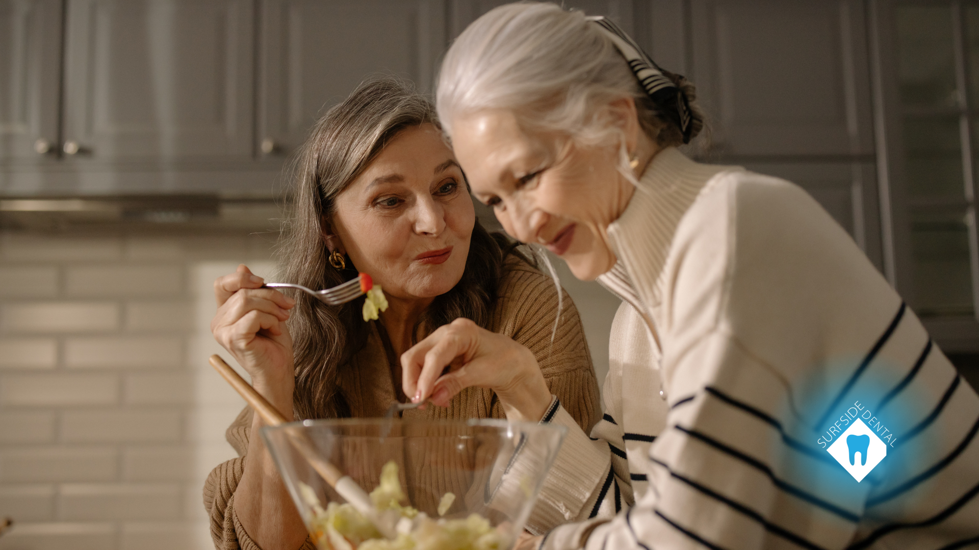 Two women are making a salad together in a kitchen.