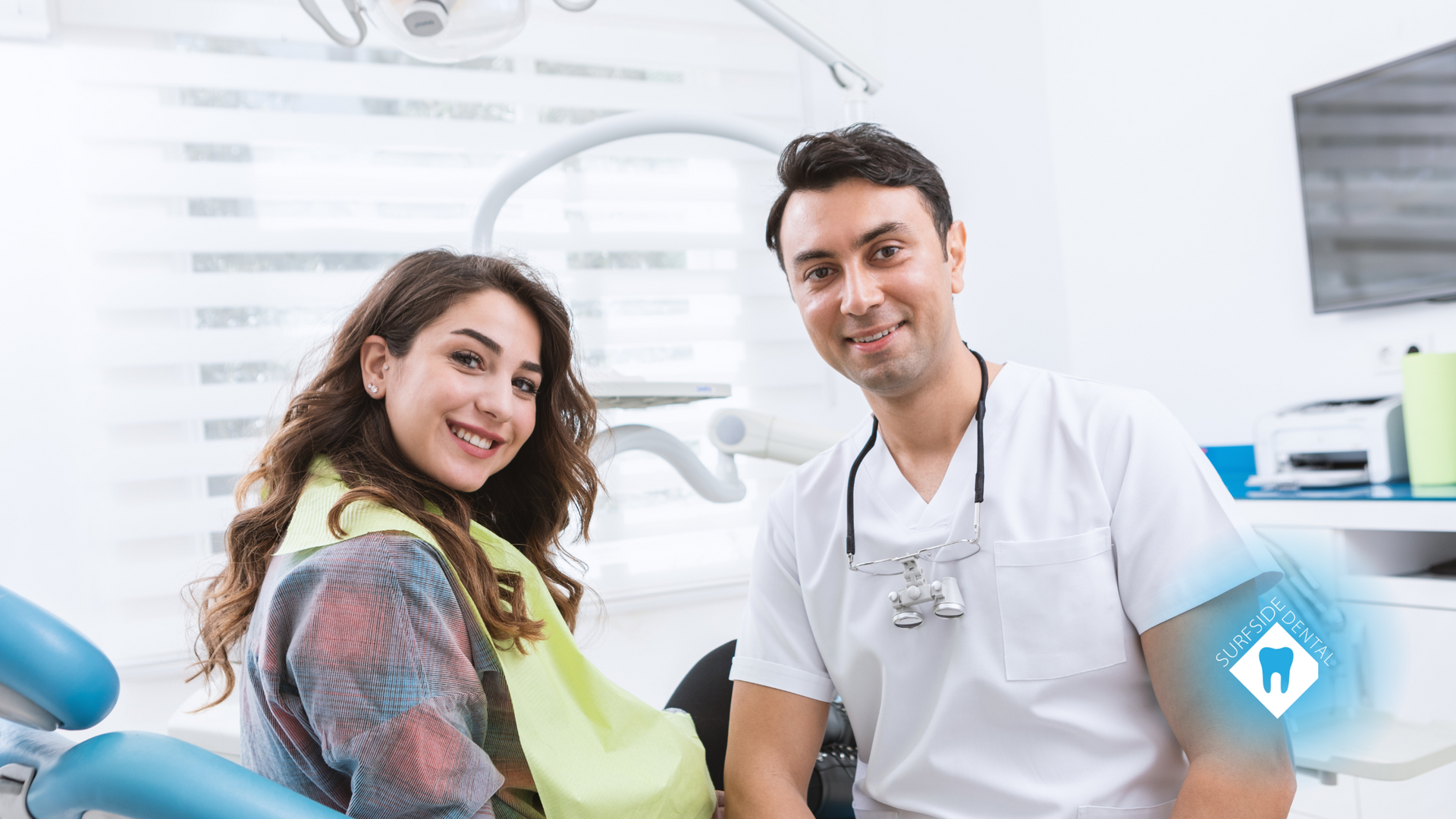 A woman is sitting in a dental chair next to a dentist.