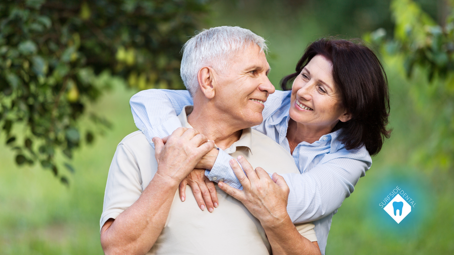 A woman is hugging an older man in a park.