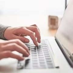 Hands typing on a laptop keyboard in a brightly lit setting.
