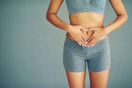 Woman in athletic wear making a heart shape over her abdomen.
