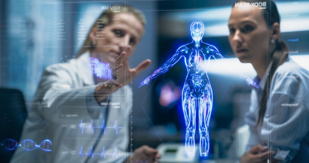 Two women examining a holographic human body scan in a lab setting.