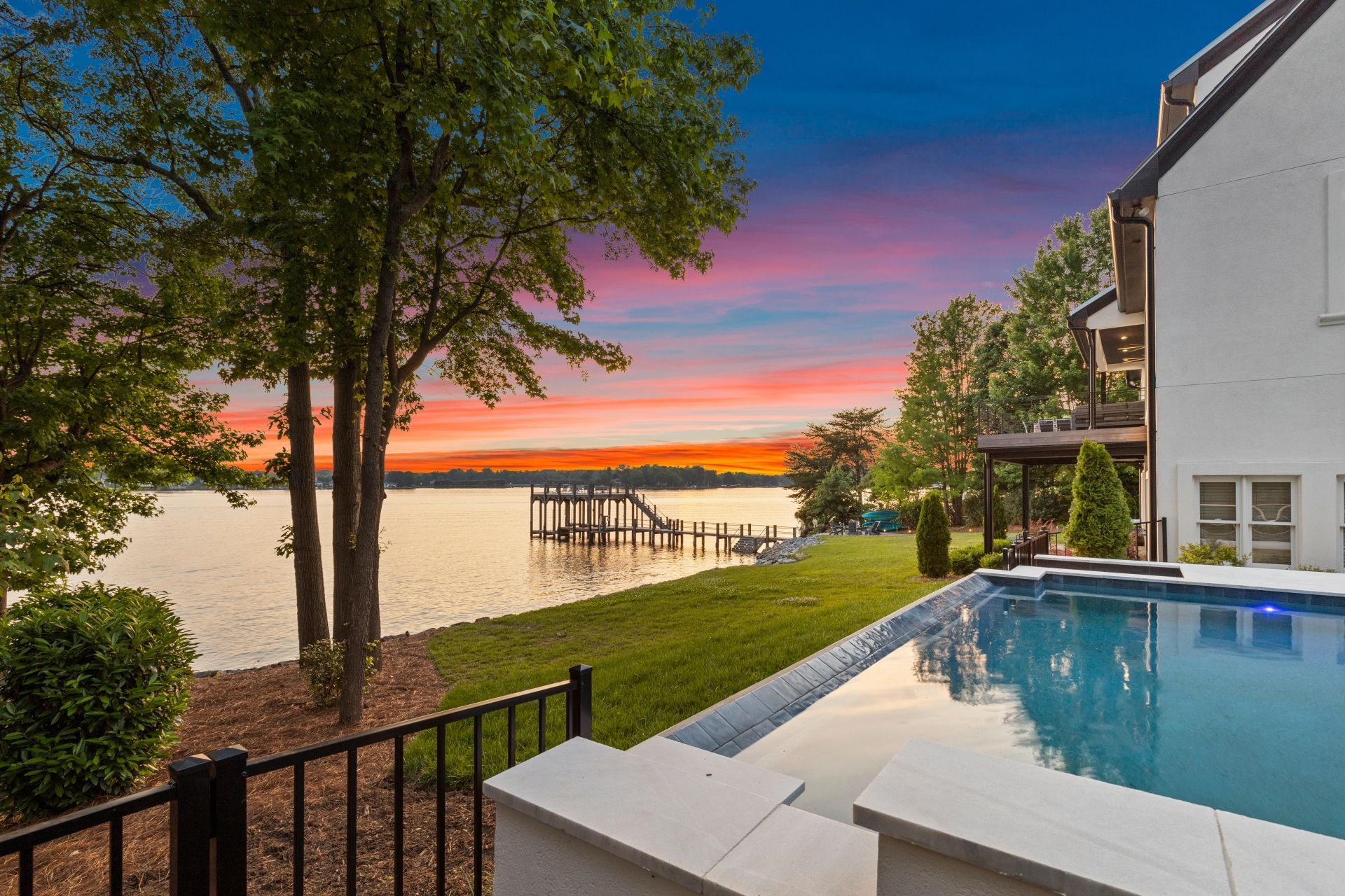 Lakeside home with a pool at sunset. Pink and orange sky reflecting in the water.