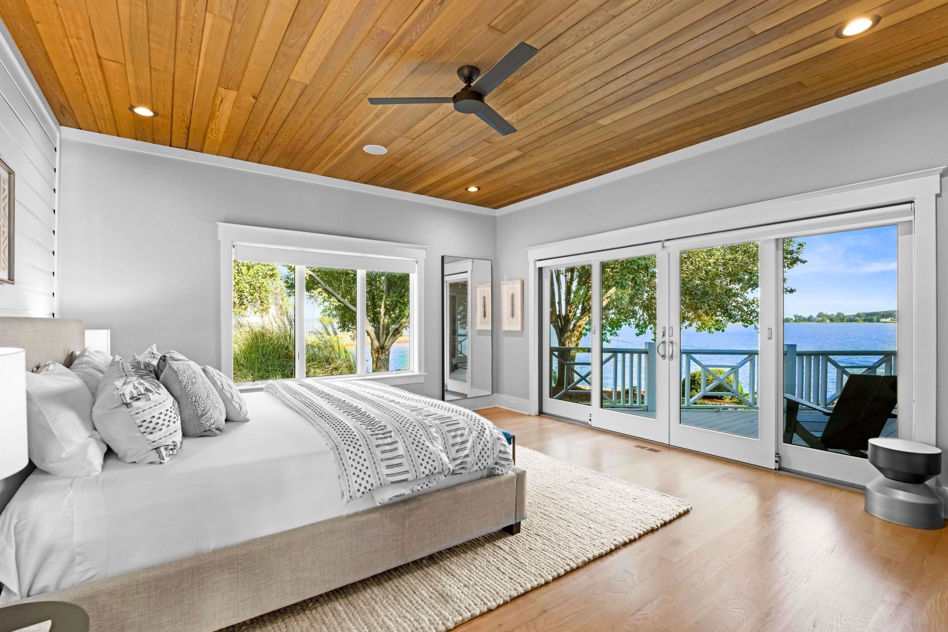 Bedroom with a wooden ceiling, large windows overlooking water, and a bed with decorative pillows.