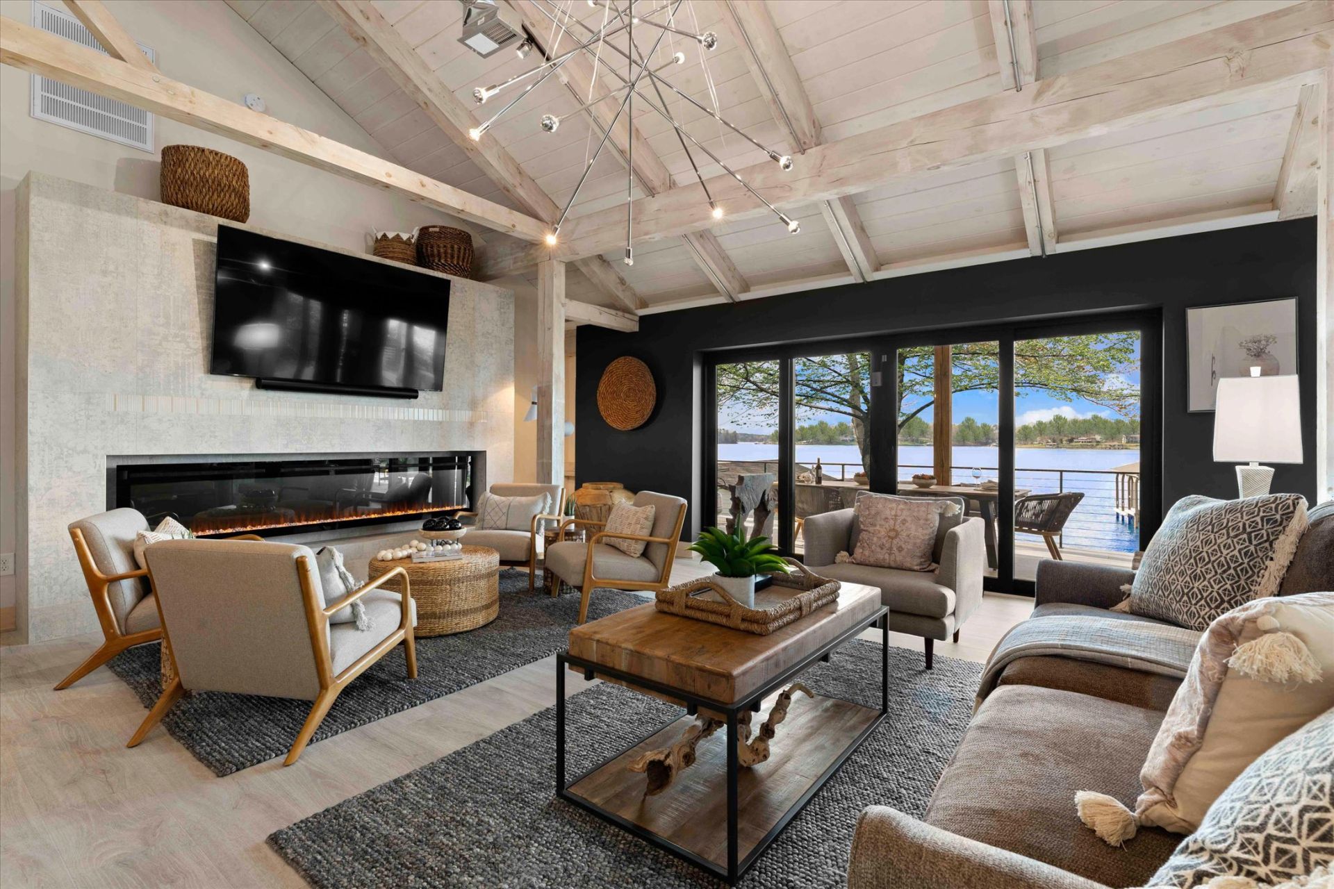 Living room with fireplace, lake view. Neutral tones, dark accent wall, vaulted ceiling, modern furniture.