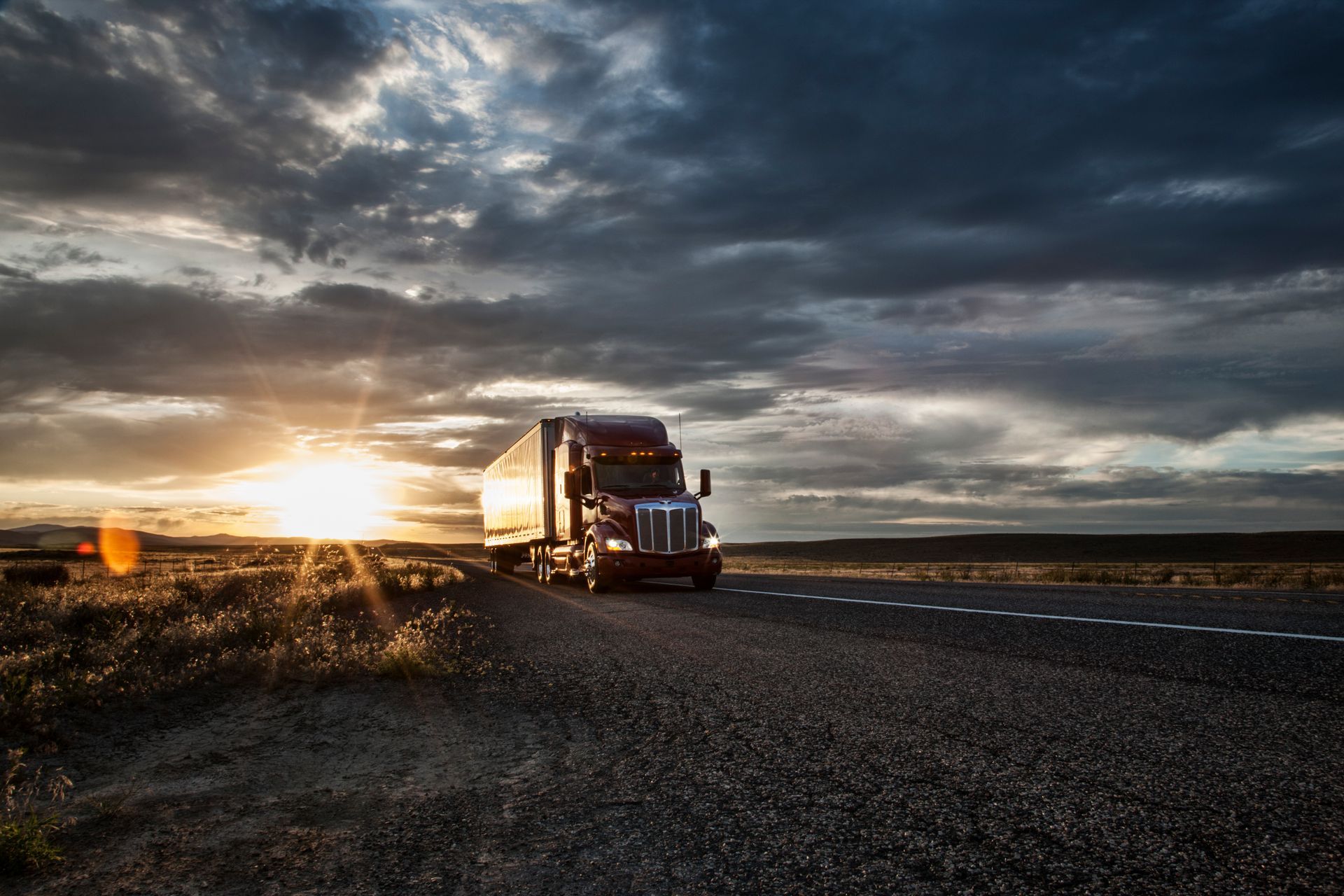 A semi truck is driving down a road at sunset.