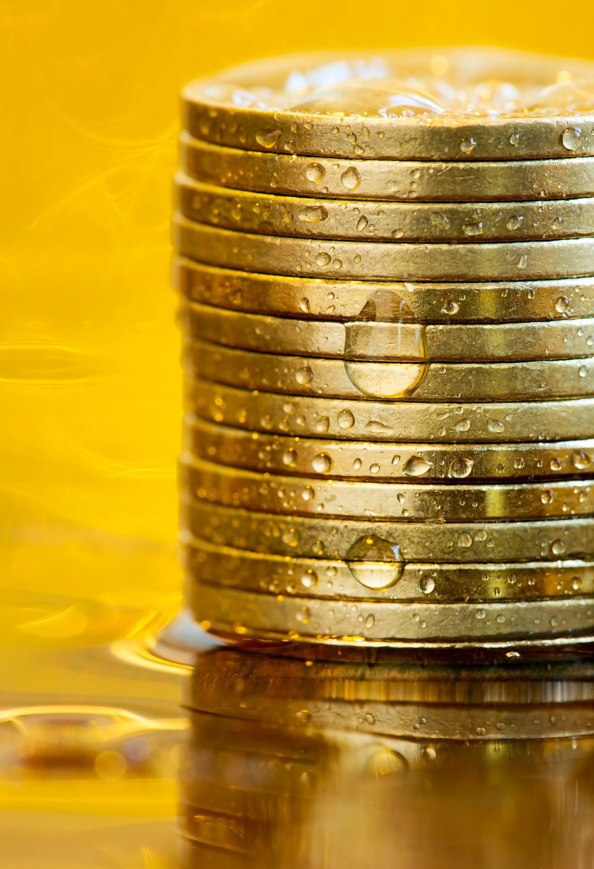 A stack of gold coins with water drops on them on a yellow background.