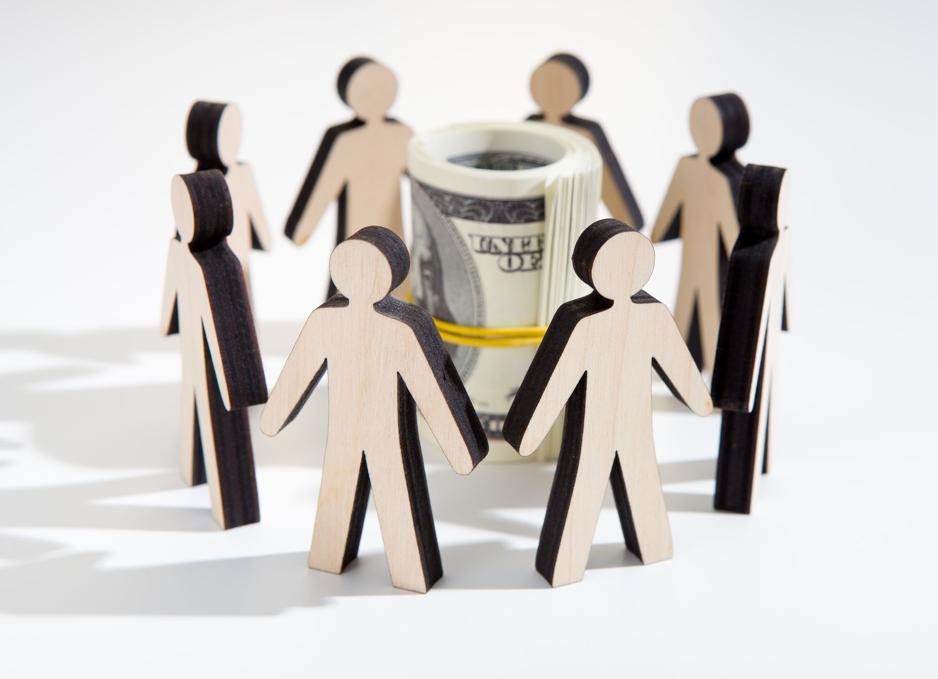 A group of wooden people holding hands around a roll of money