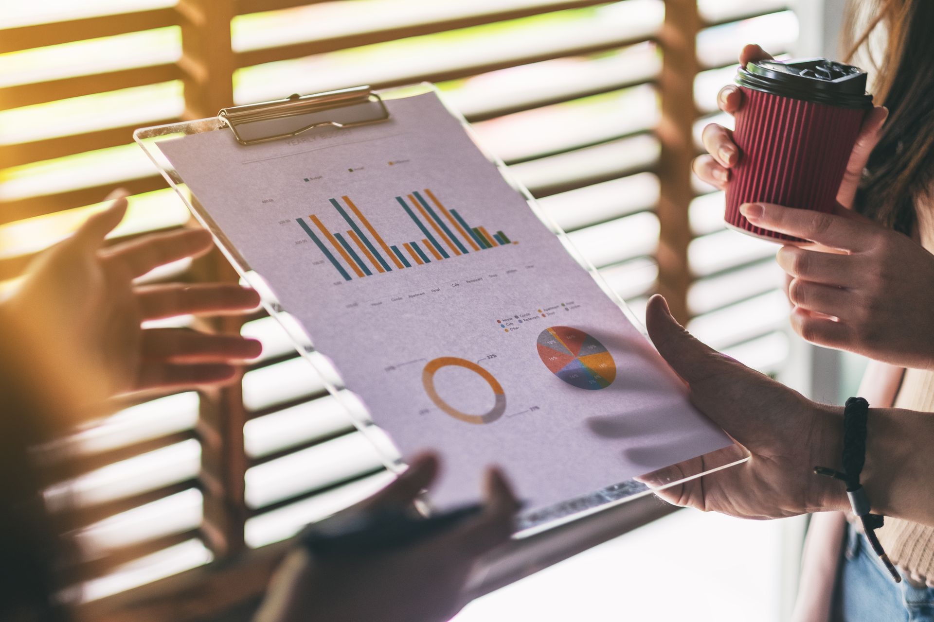 A woman is holding a cup of coffee and looking at a clipboard with a graph on it.